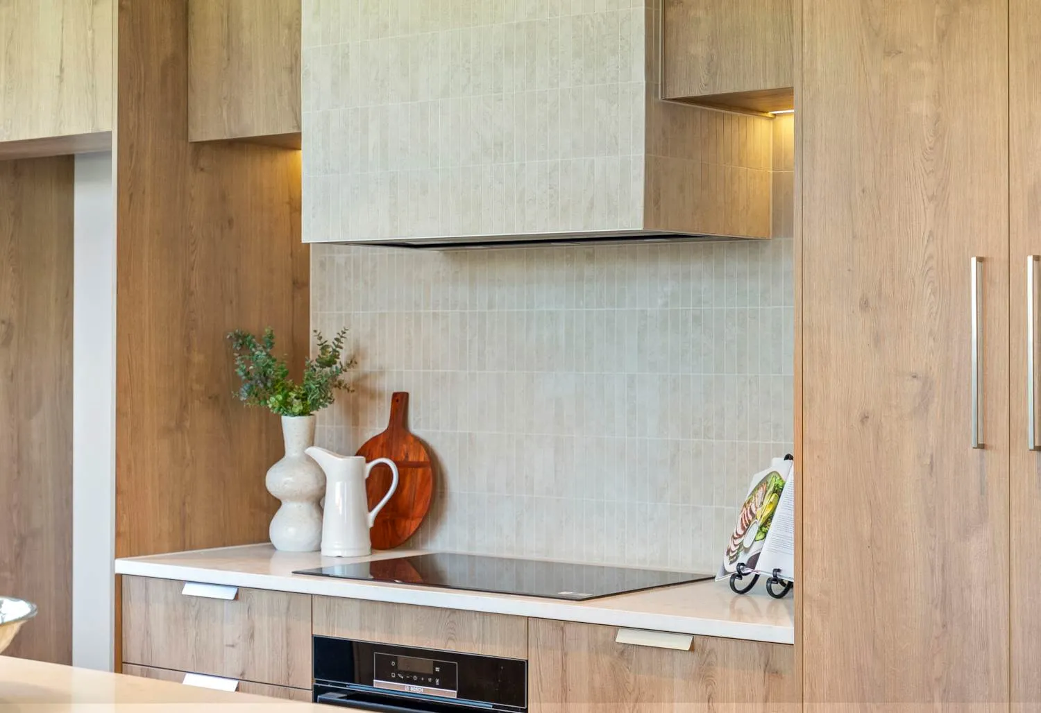 A close view of the cooktop, splashback and extractor set into timber cabinetry, with a jug and board on the bench.
