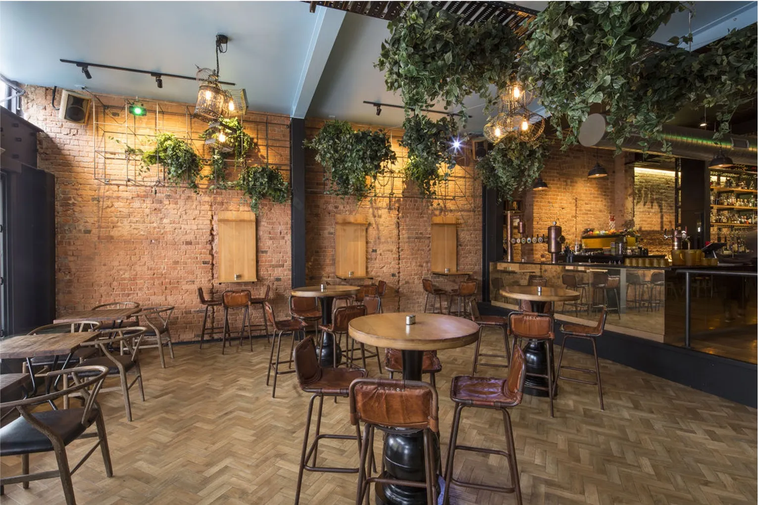 A larger dining room with brick walls, planting suspended from the ceiling and the bar visible at the far end.