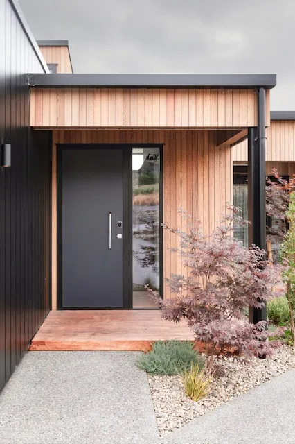 A closer view of the entry, showing the cedar lining meeting the dark vertical cladding and the planting at the threshold.