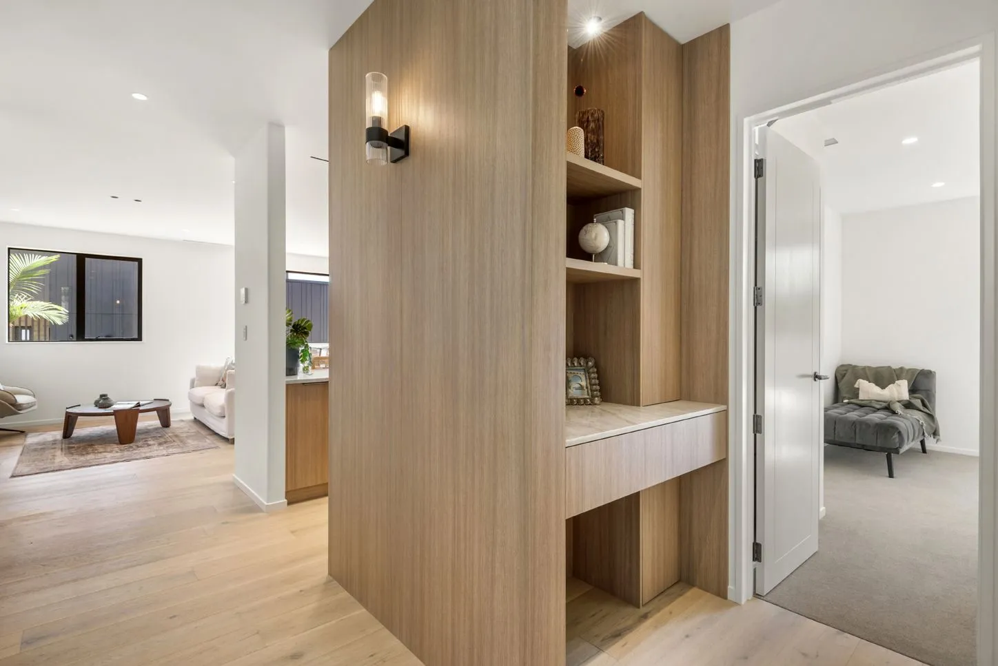 Entry joinery in pale timber with open shelving and a bench, framing sightlines through to the lounge and a bedroom.