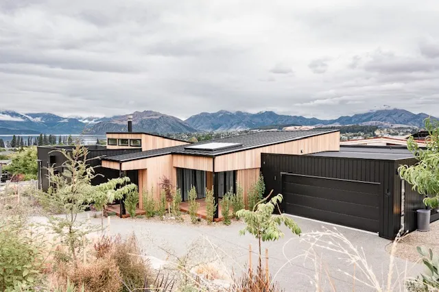 The house seen from above, showing its long roof planes, the garage and planting, with mountains in the distance.
