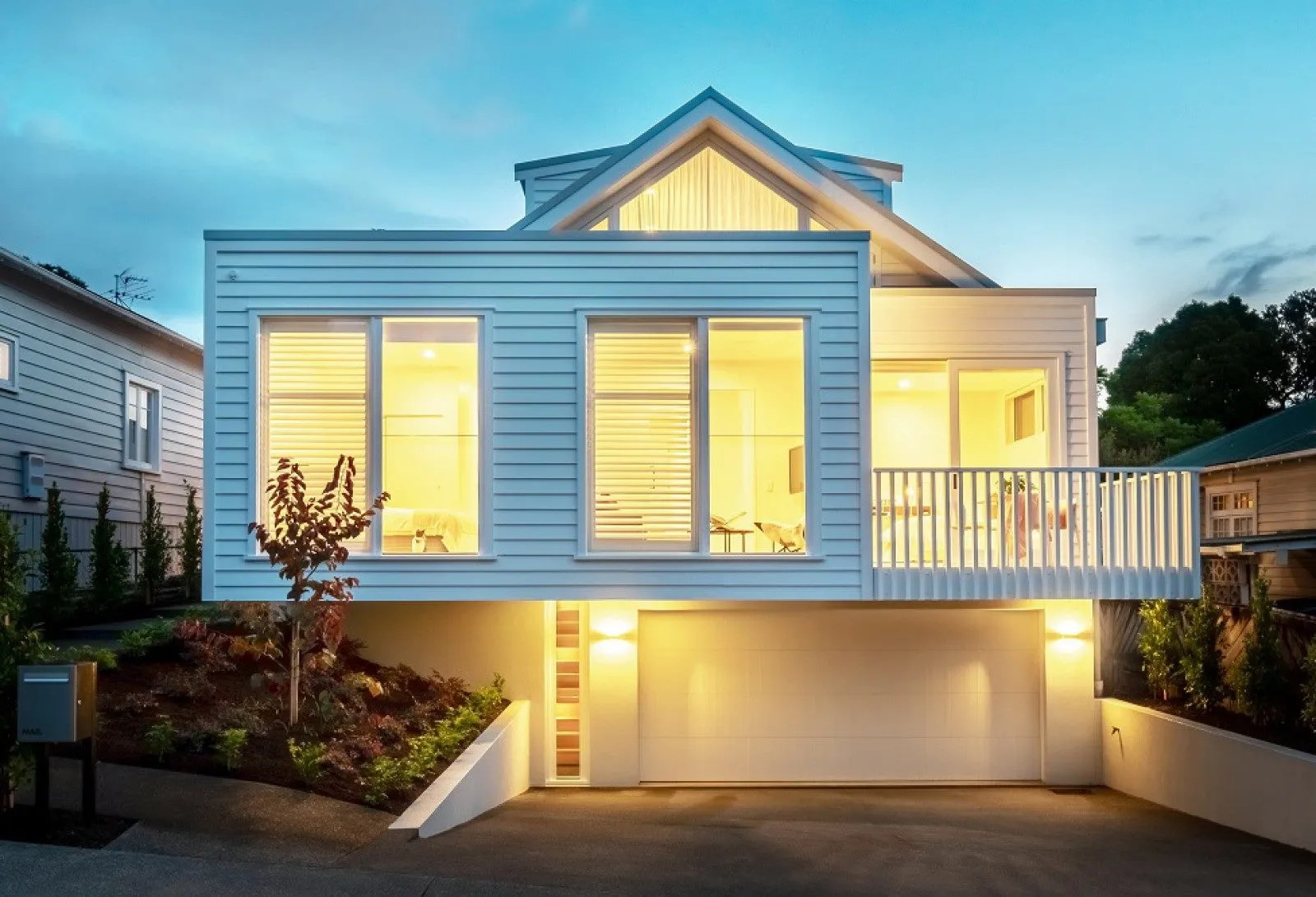 The front of the house at night, its weatherboard elevation and planting lit from below.