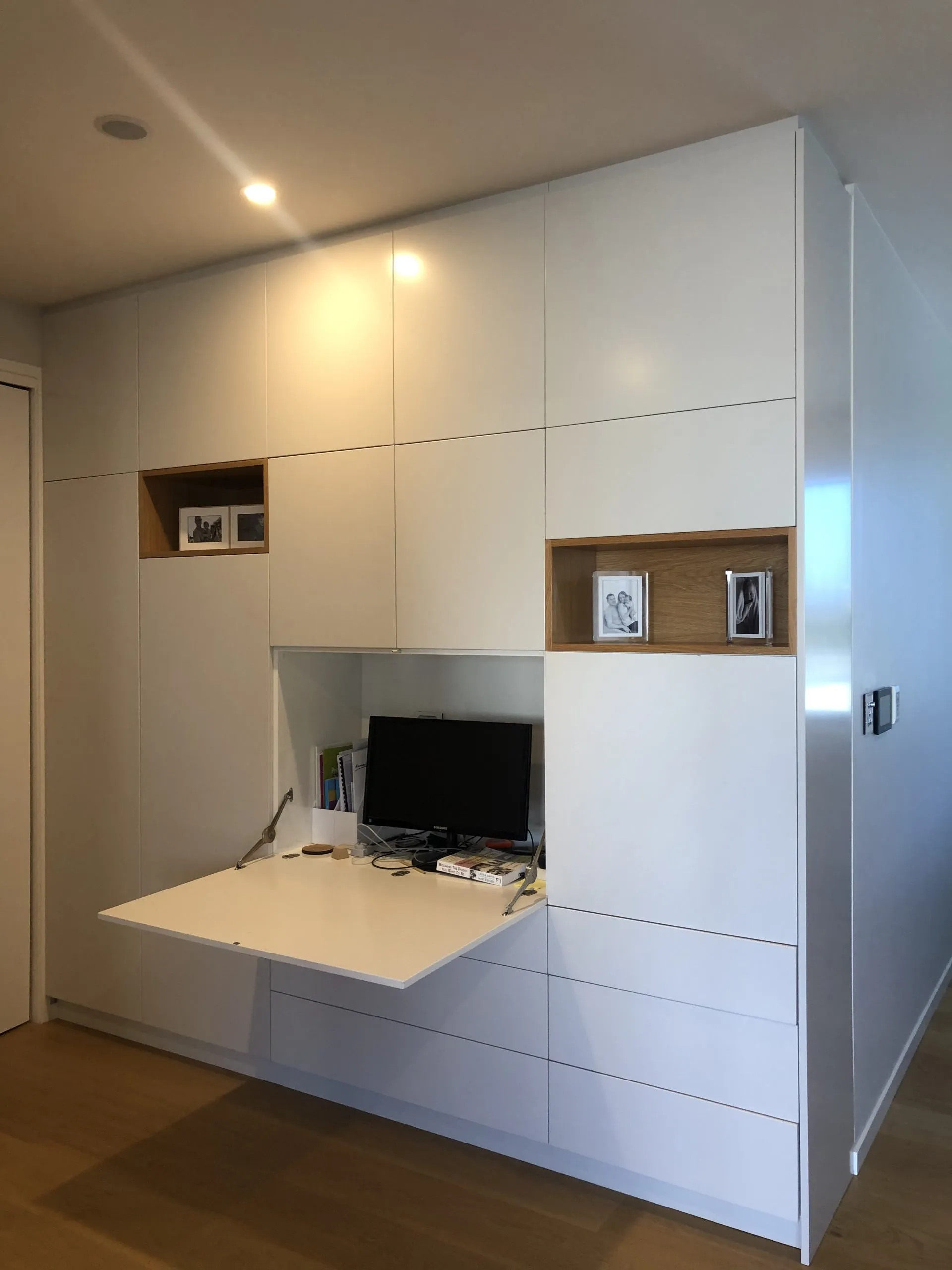 The same joinery wall with a fold-down desk open, showing how the storage conceals a working surface and screen.