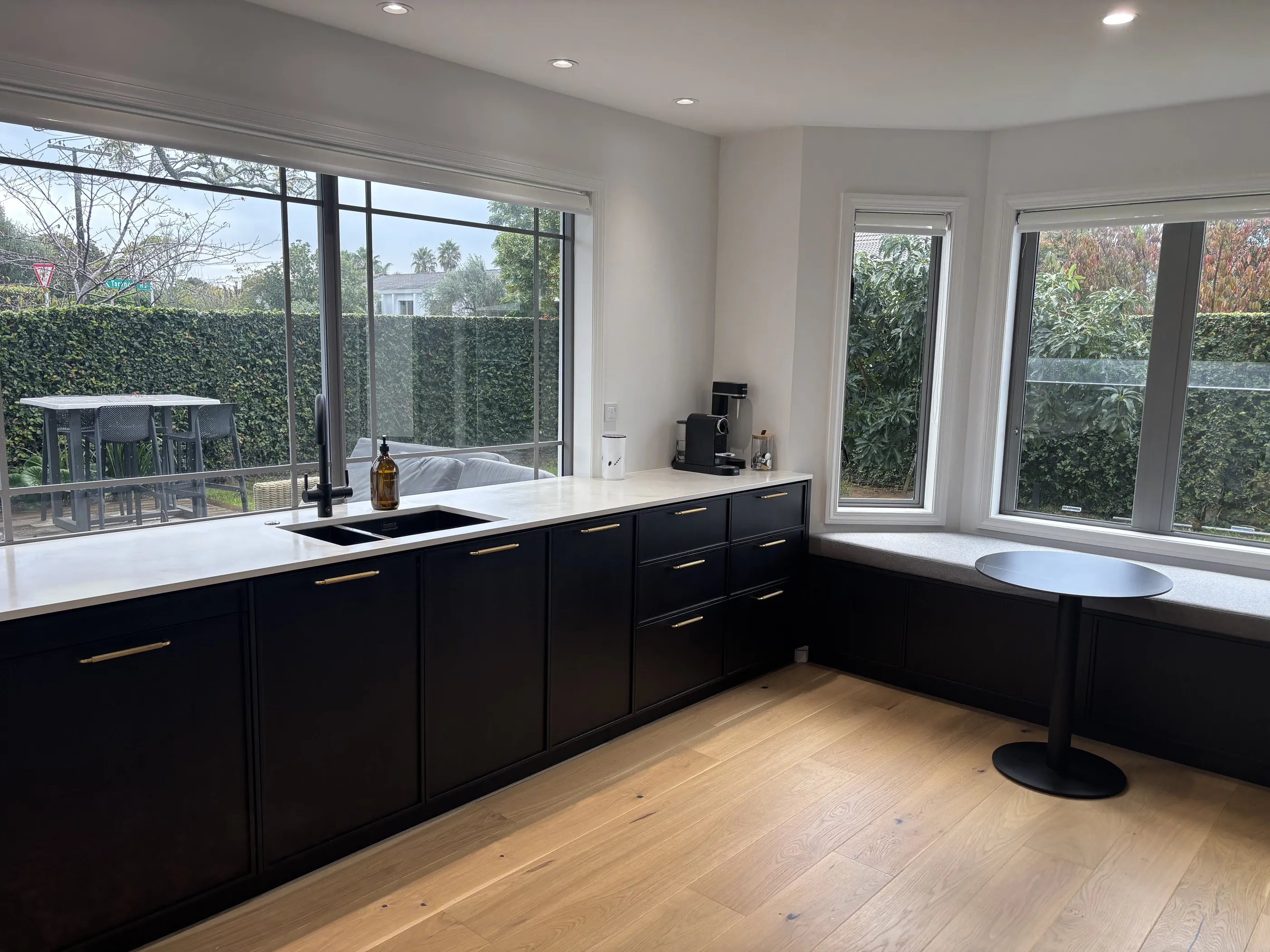 The kitchen from the far end, with black cabinetry wrapping into a bay window and a round table set in the corner.