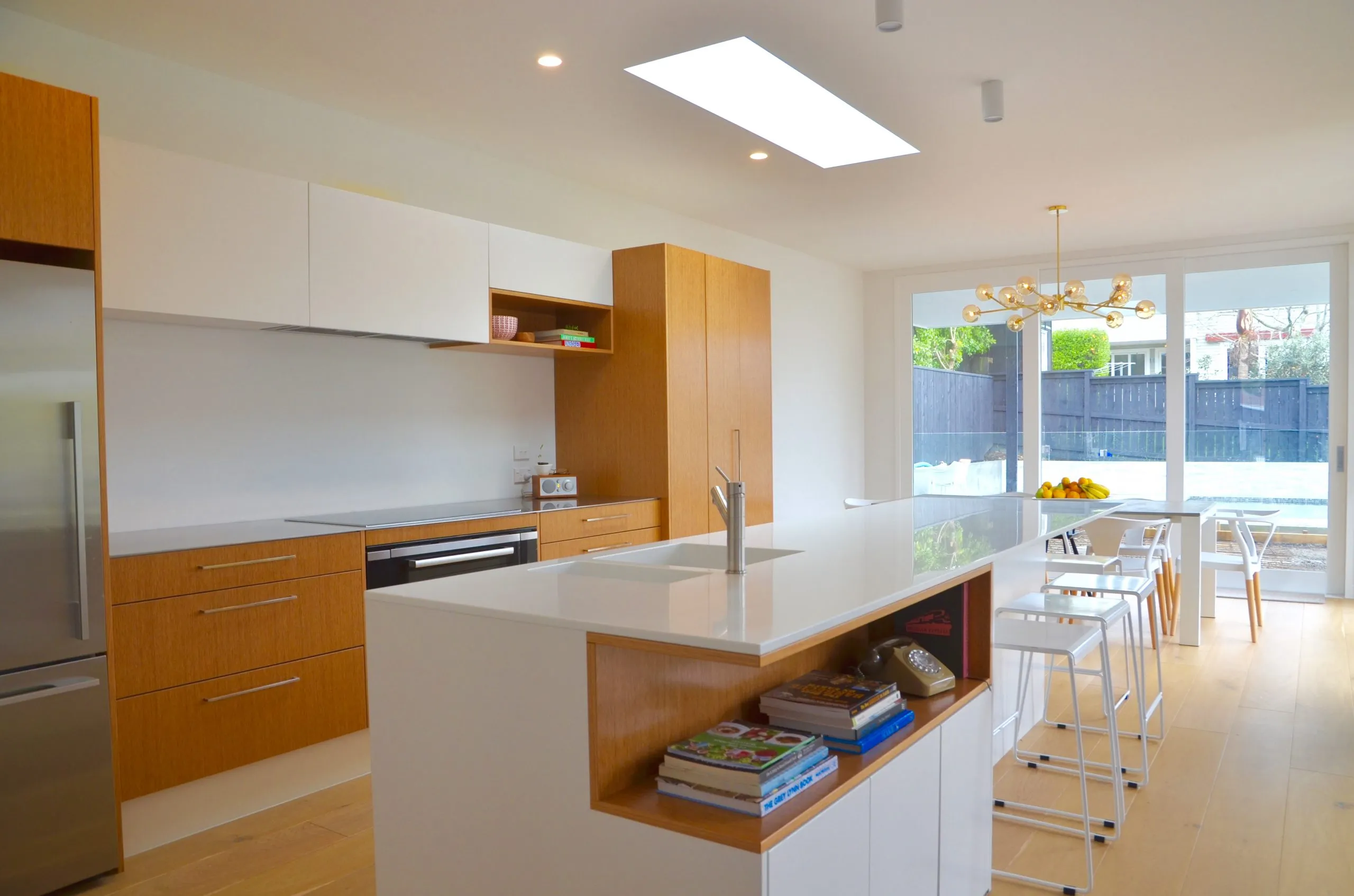 The kitchen island seen from the dining end, with oak joinery, integrated appliances and a skylight above.