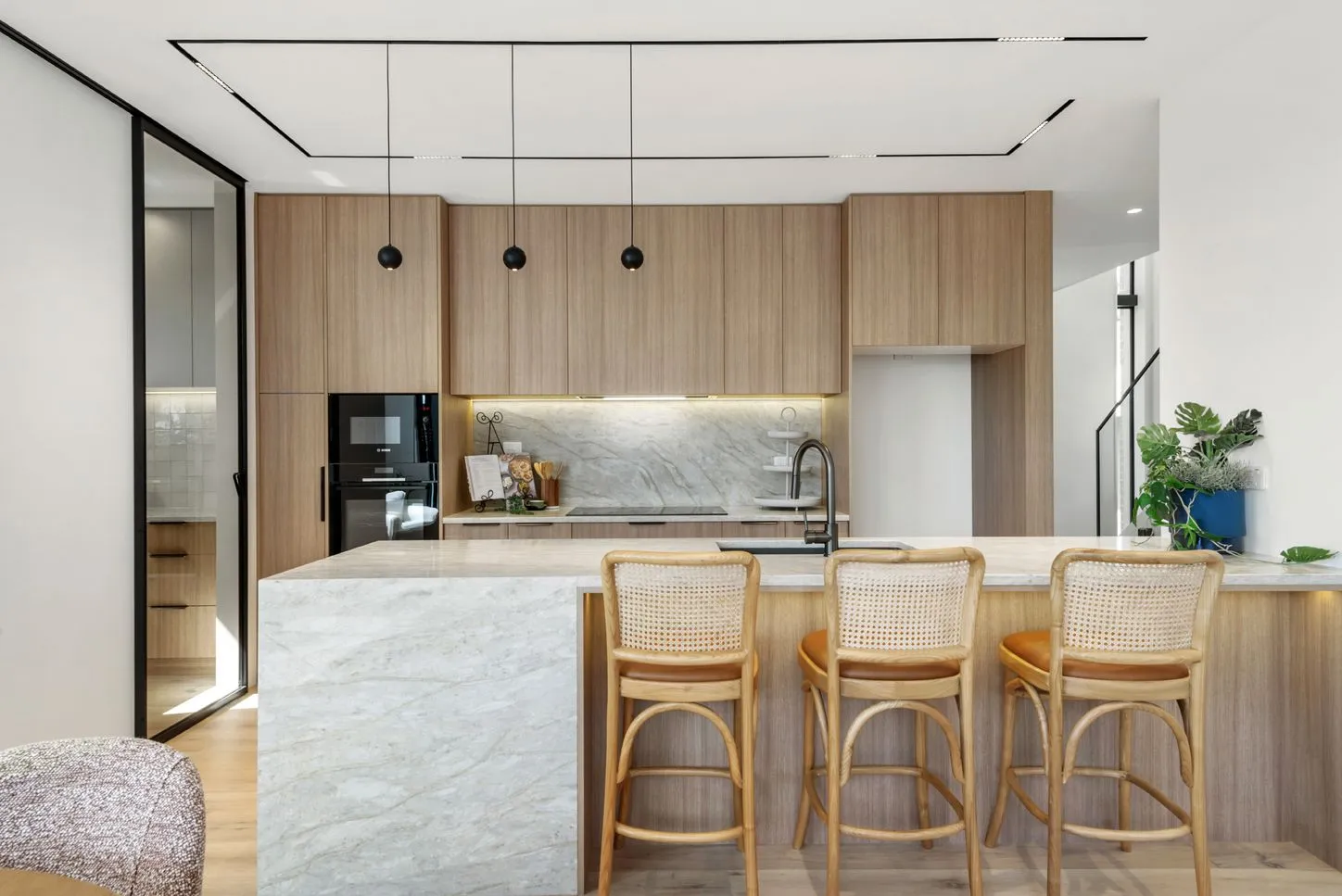 The kitchen seen straight on, with a black linear track light across the ceiling and a stone benchtop running the length of the joinery.