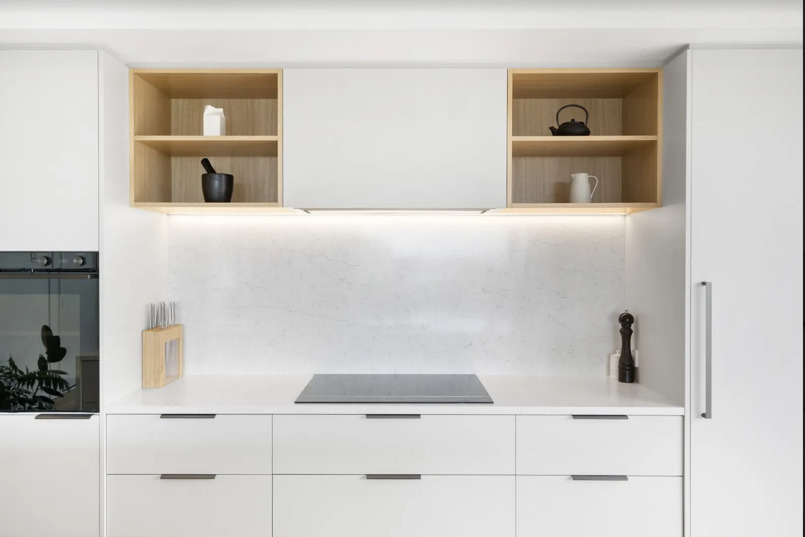 A run of white cabinetry with oak niches above the benchtop, an induction cooktop and an integrated oven.