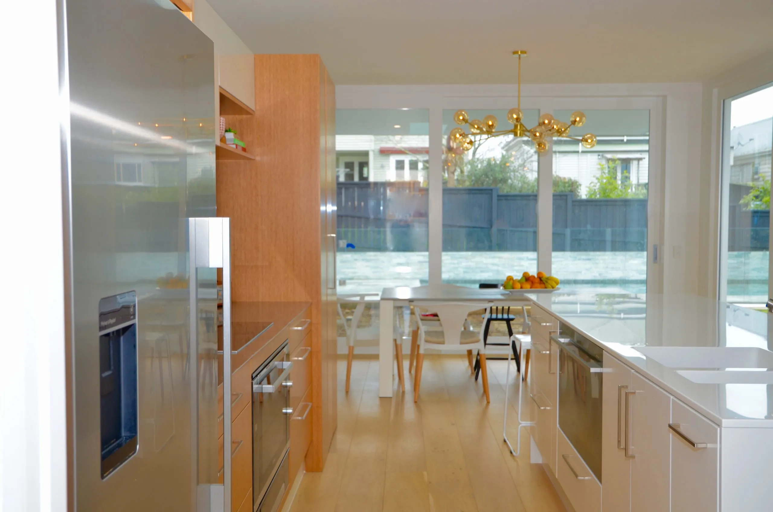A kitchen with a white stone island and bar stools against a run of oak cabinetry, opening to the living area beyond.