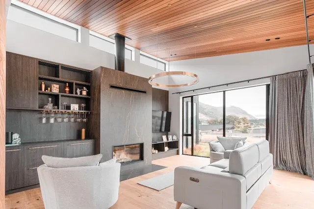 The same living room from the opposite side with the fire lit, timber bar joinery along one wall and glazing to the view.