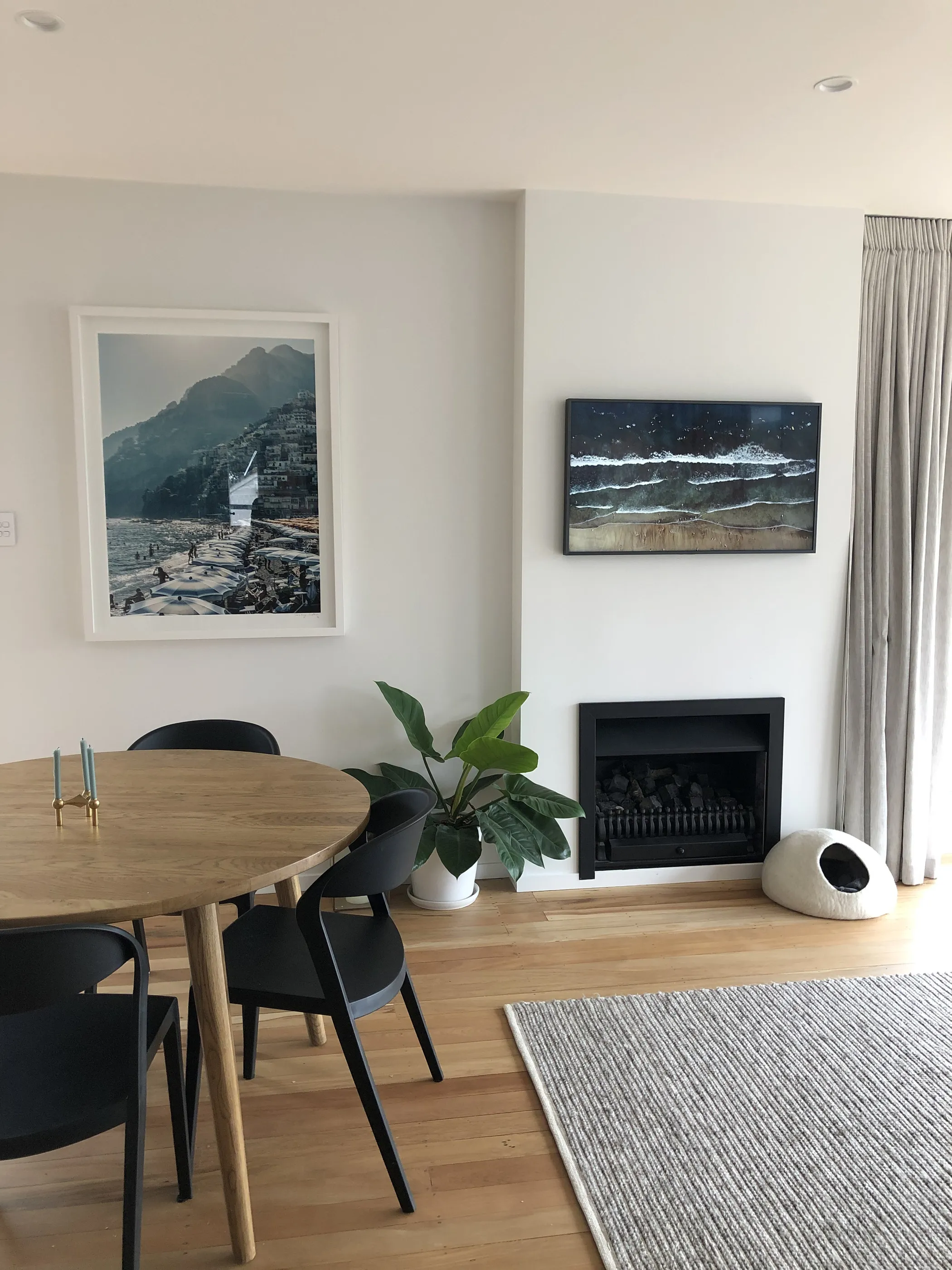 A living and dining space with a fire set into the wall, framed artwork alongside and a round oak table.