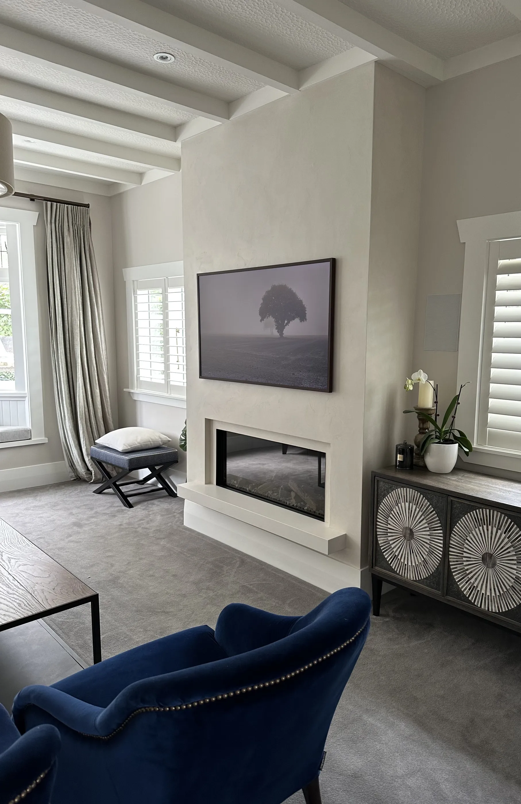 A living room with a plastered fireplace surround running floor to ceiling, an inset fire, and a navy velvet armchair alongside.