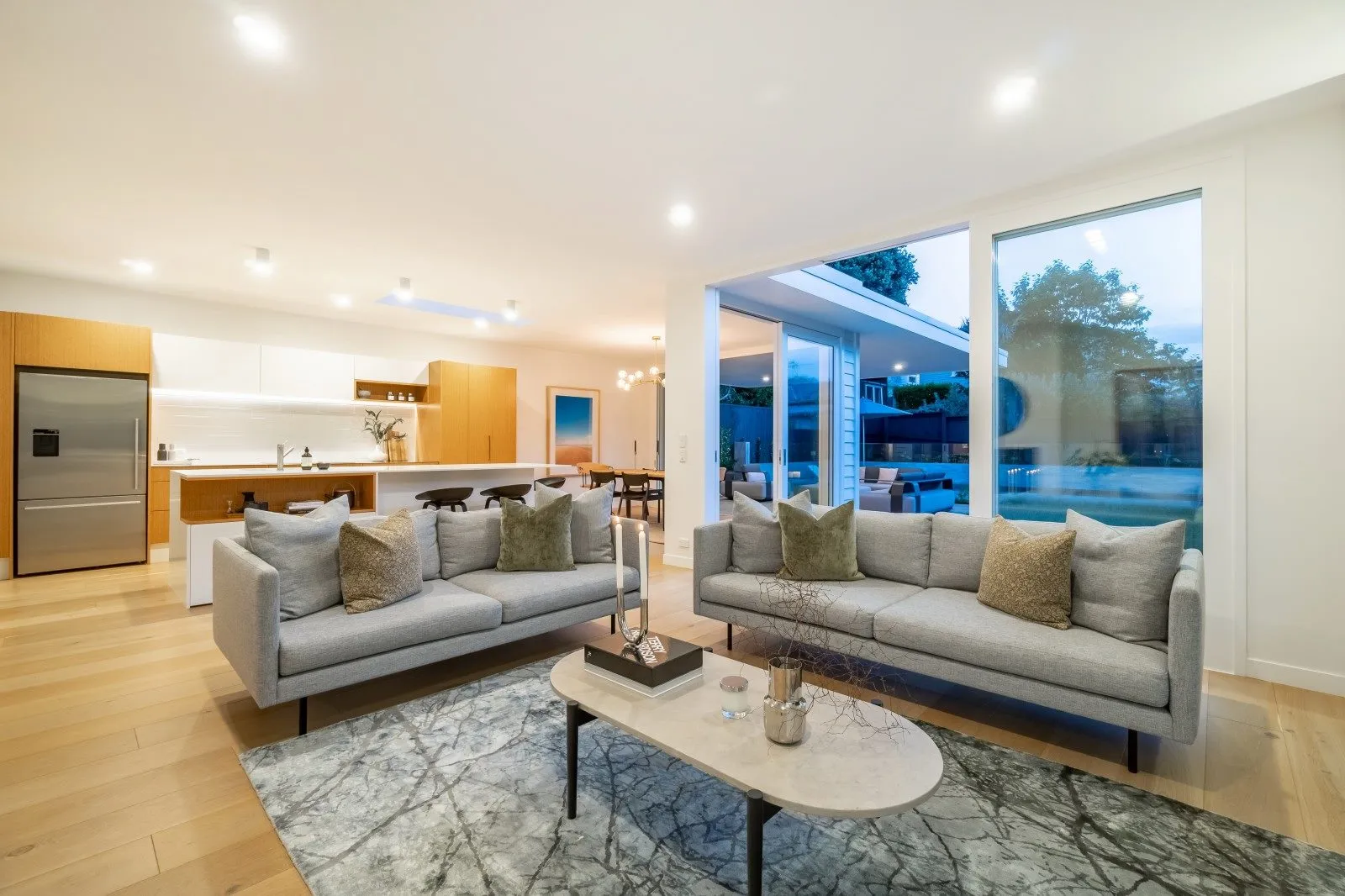 A living room with pale sofas and a low table, glazing folded back to the pool and terrace outside.