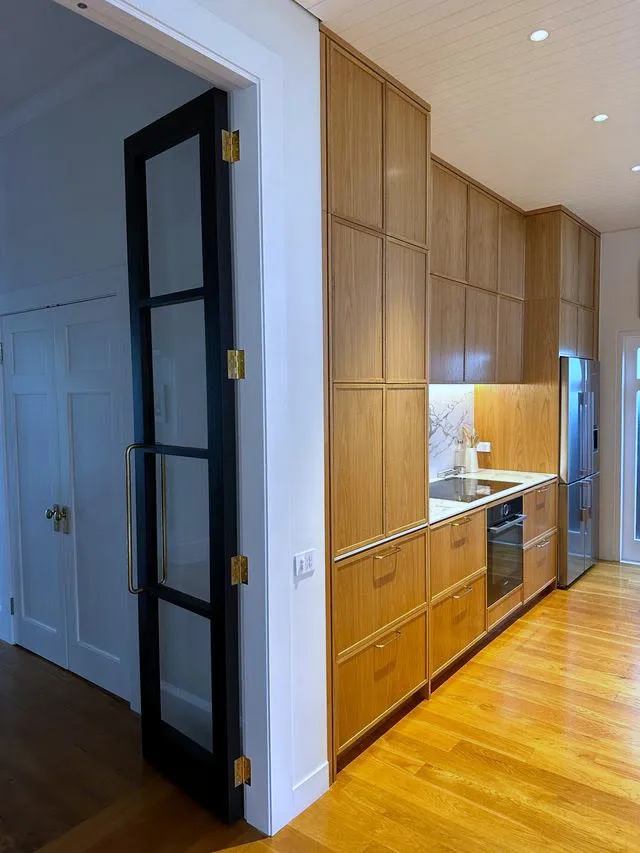 A black steel-framed glass pocket door set into oak joinery, sliding back to open the kitchen through to the next room.