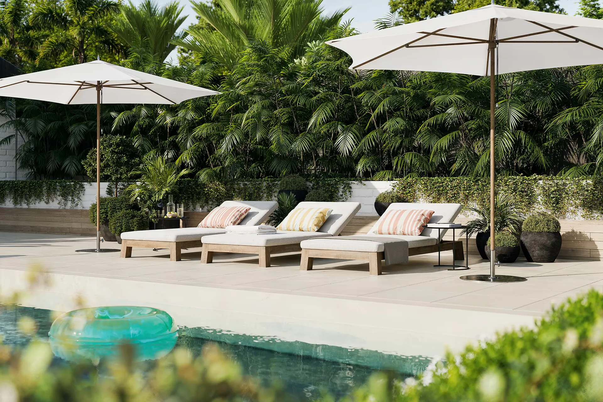 A shared pool with timber loungers, cream umbrellas and dense palm planting around the perimeter.