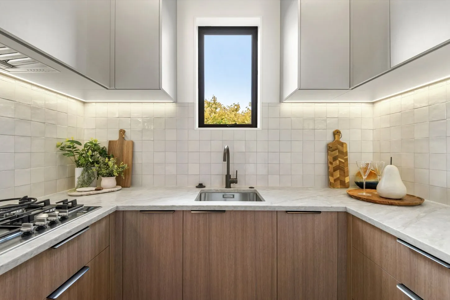 A scullery with white overhead cabinetry, a timber base run and a window set above the sink.
