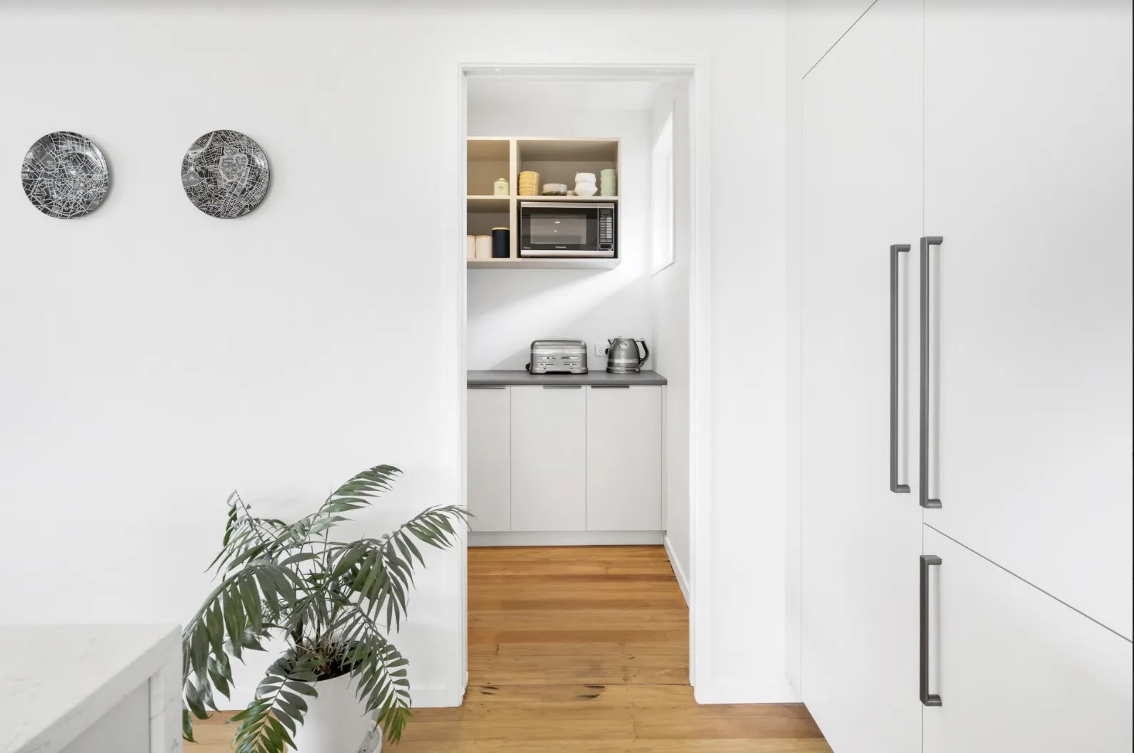 A walk-in scullery seen through the opening from the kitchen, with a bench and shelving inside.