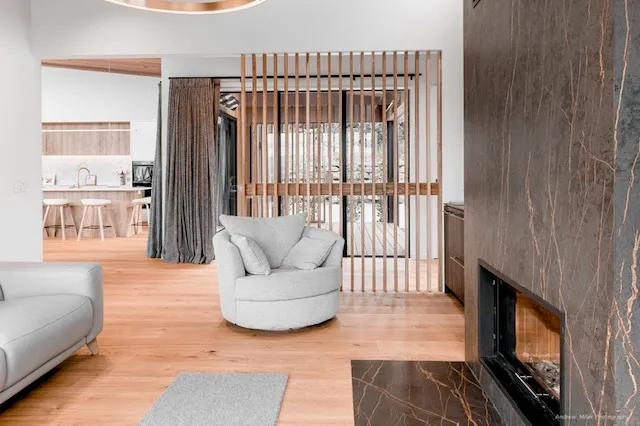 A timber screen wall of vertical battens dividing the living space from the kitchen beyond, with light passing between the slats.