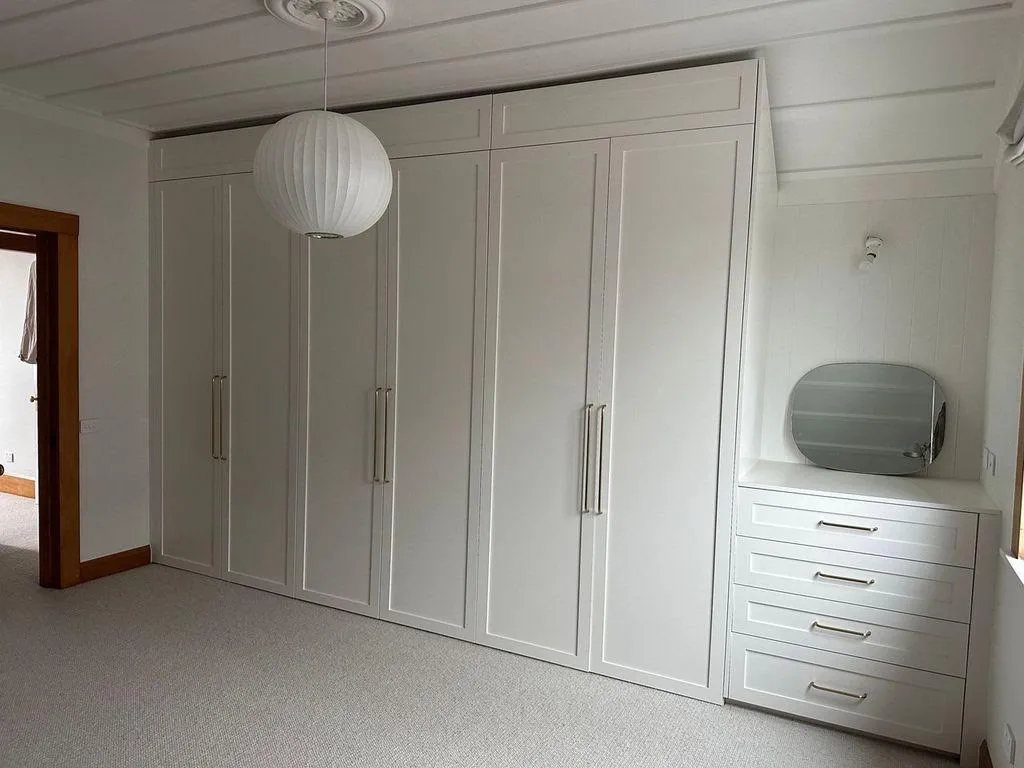 Built-in white shaker wardrobes with brass handles, running the full height of a carpeted bedroom wall.